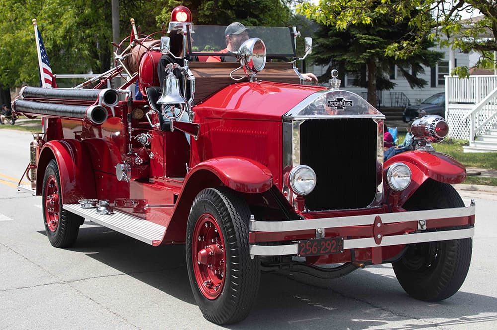 An old-fashioned fire truck driving down the road for a parade.