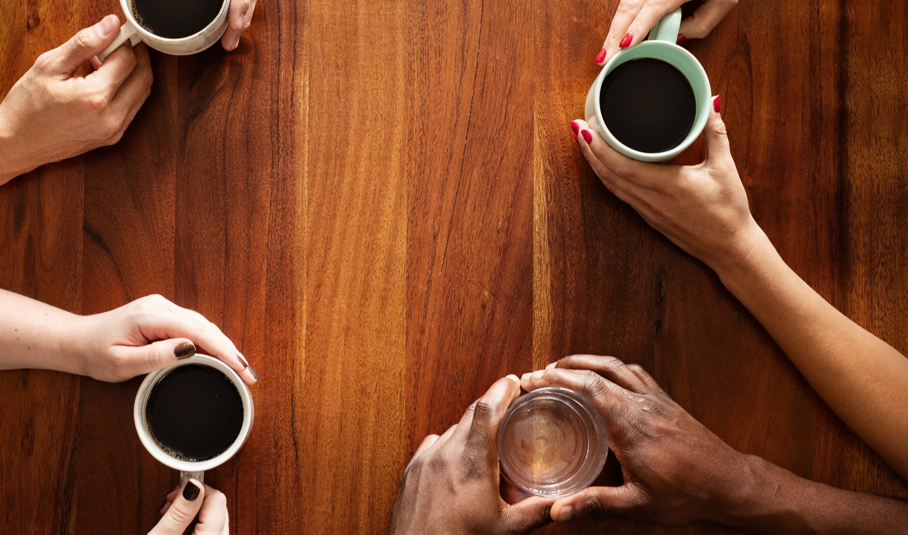 Diverse group of people having coffee. Top view of hands holding coffee cups. Coffee meeting with diverse hands. Coffee and conversation among diverse group of pleple. Diverse people drinking coffee